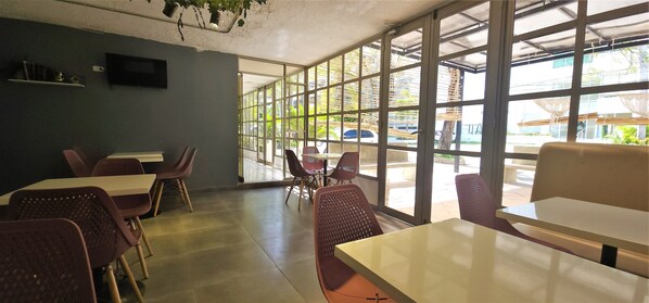 Un café avec des tables et des chaises, de grandes fenêtres et une vue sur l’extérieur.