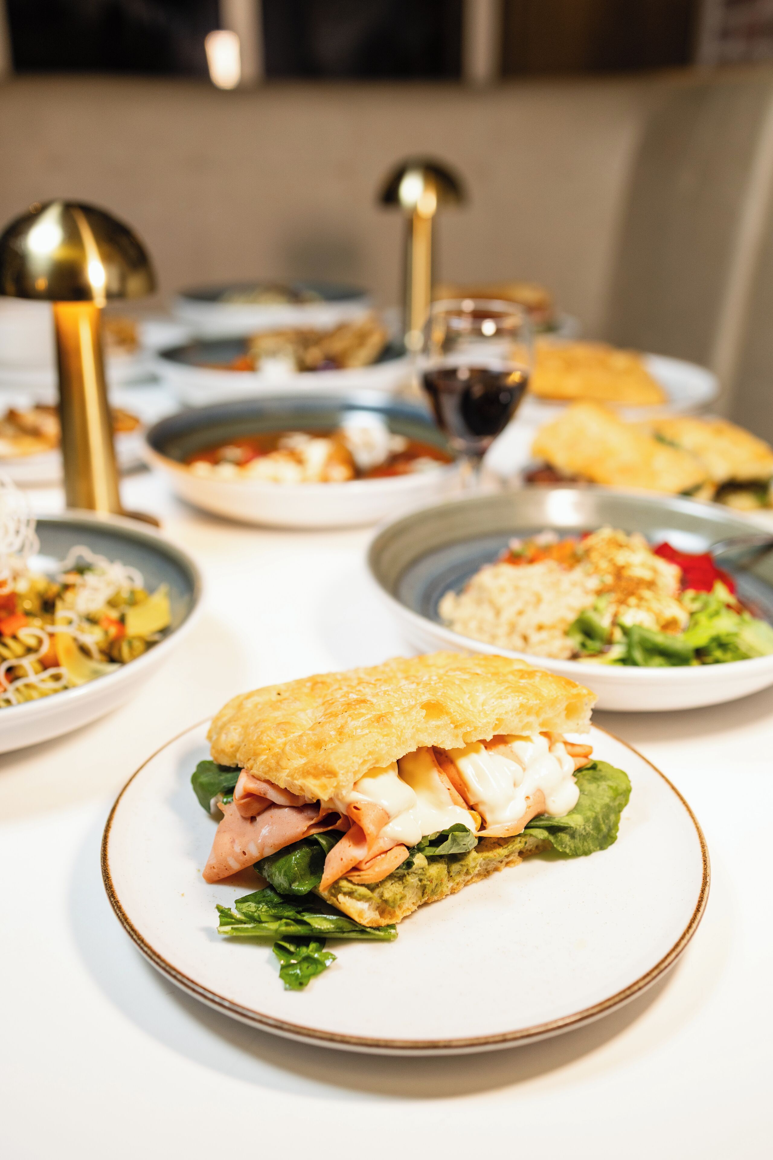 A dining table with various dishes, including a sandwich with greens and meat, and a bowl of salad.