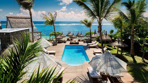 A poolside area with lounge chairs, a swimming pool, and a view of the ocean.