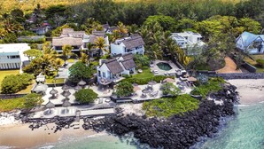 An aerial view of a coastal resort with multiple buildings, a swimming pool, and a rocky shoreline.