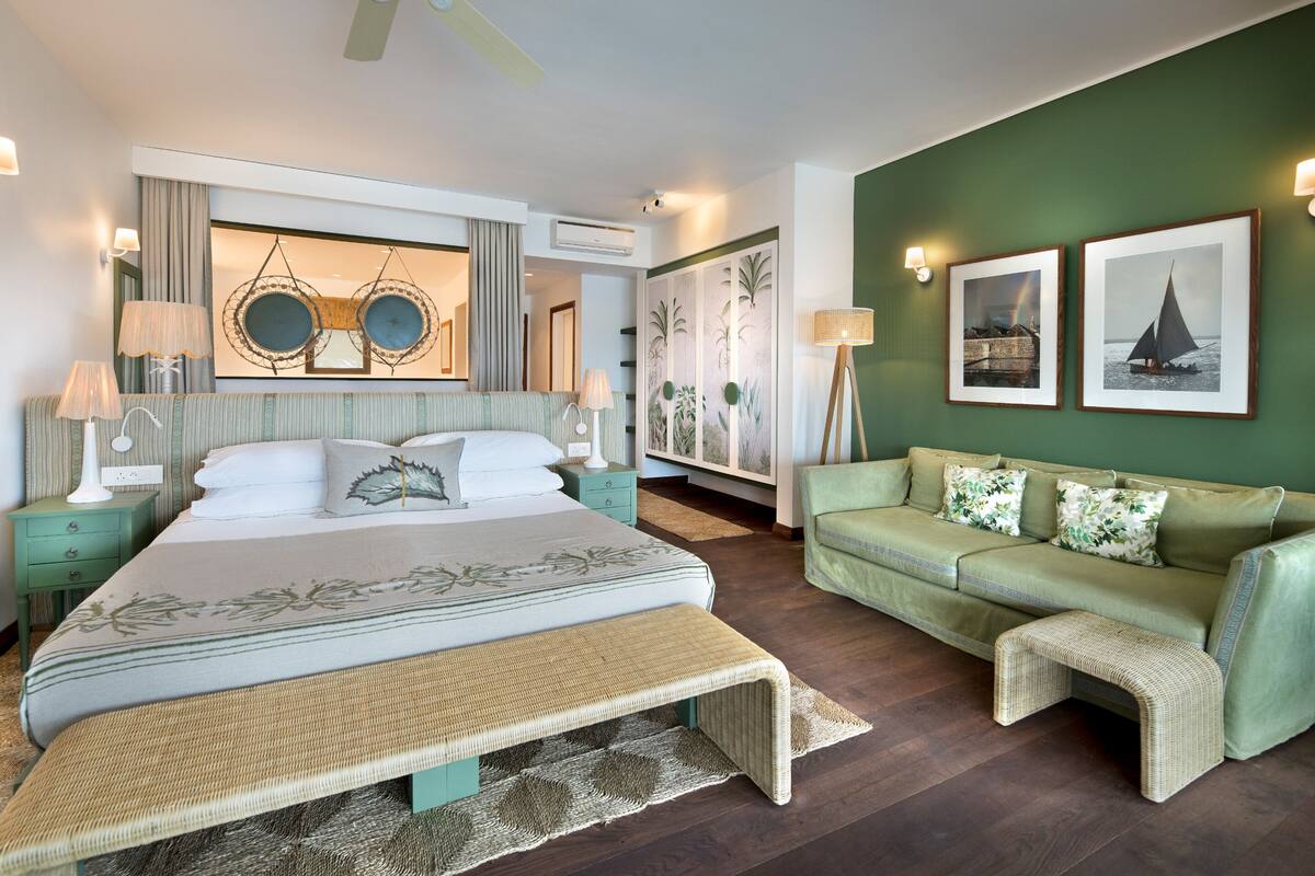 A bedroom with a bed, a green sofa, a standing lamp, and framed pictures on the wall.