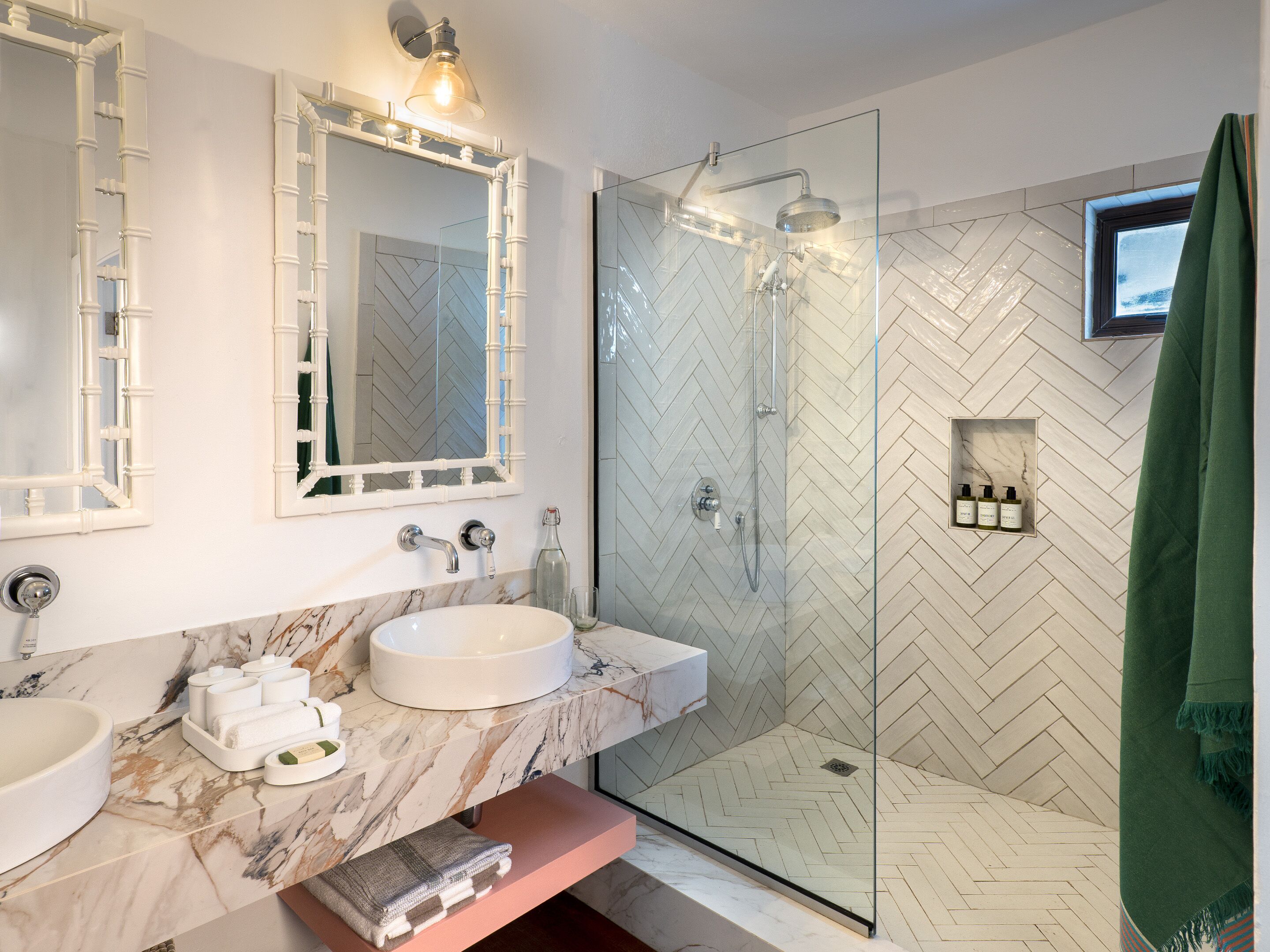 A modern bathroom with a marble sink, a glass-enclosed shower, and a herringbone-patterned tiled wall.