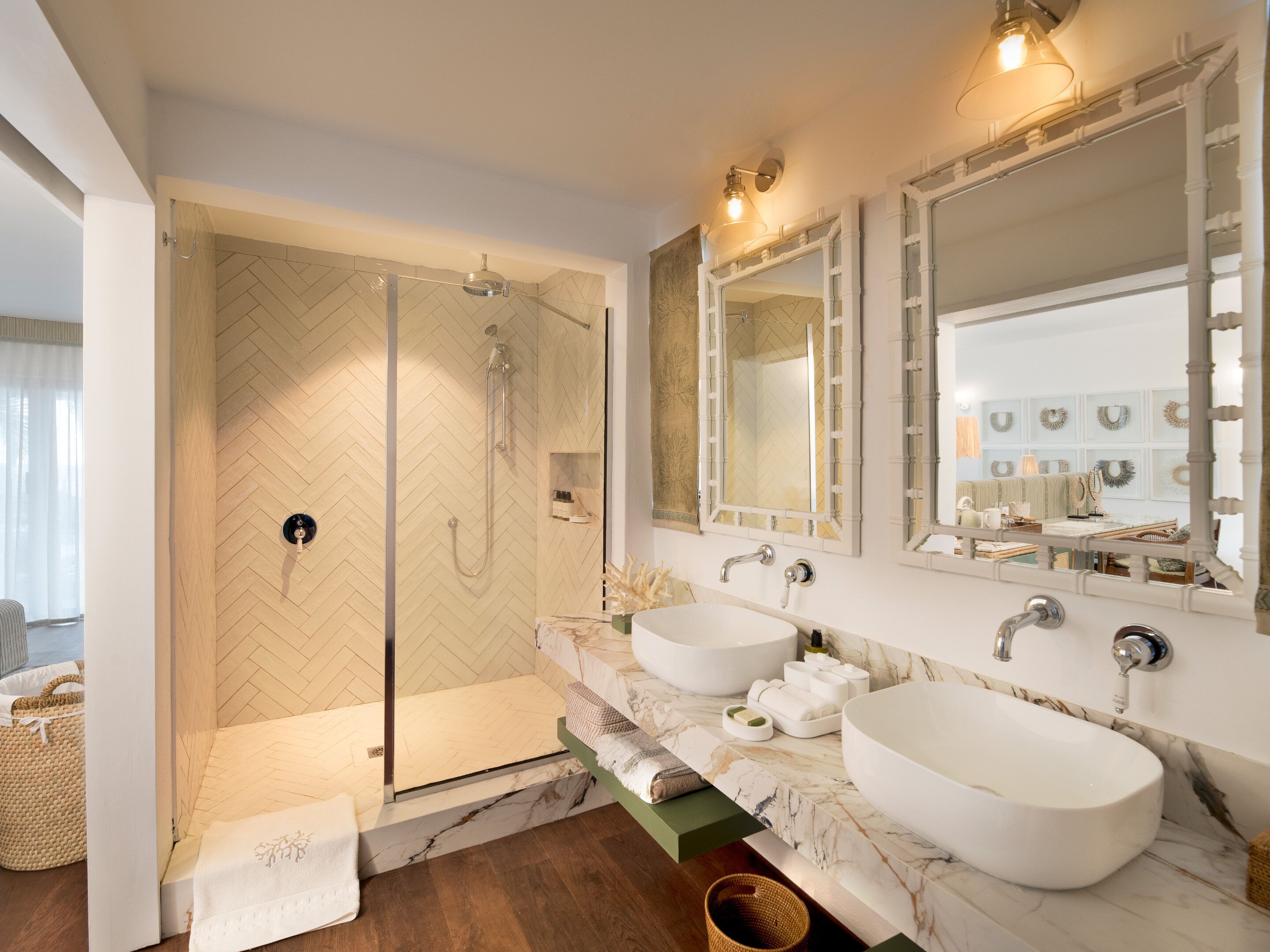 A modern bathroom with a herringbone-patterned shower wall, two large marble sinks, and a walk-in shower.