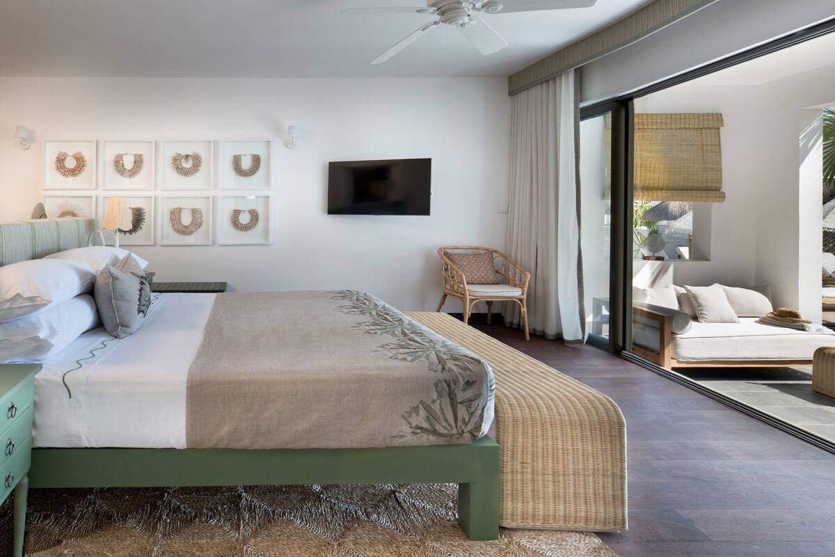 A bedroom with a bed, a chair, a television, and a balcony with a view.