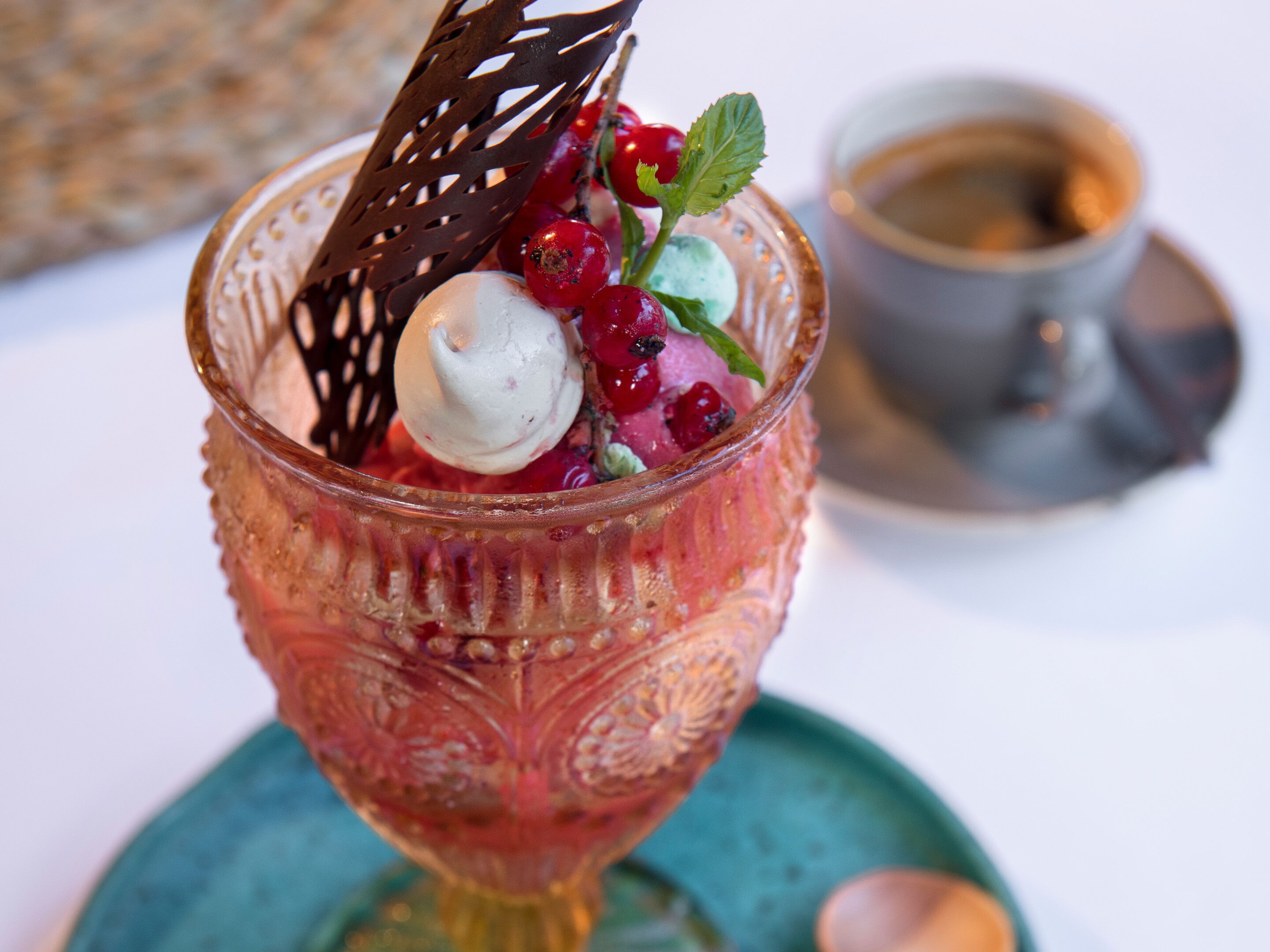 Ein Dessert in einer verzierten Schale mit Beeren und einer Kugel Eis, dazu eine Tasse Kaffee auf einem Untertasse.