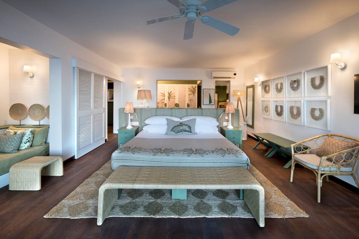 A bedroom with a bed, bedside tables, a chair, a bench, and a ceiling fan.