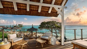 A wooden deck with wicker furniture, a thatched roof, and a view of the ocean.
