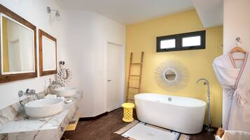 Ein Badezimmer mit einer großen Badewanne, zwei Waschbecken mit Marmorplatten, einer Holzleiter und einem Spiegel in Form einer Sonne an der Wand.