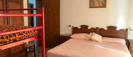 Un dormitorio con una cama litera, una cama individual, un armario de madera y una puerta que da a otra habitación.