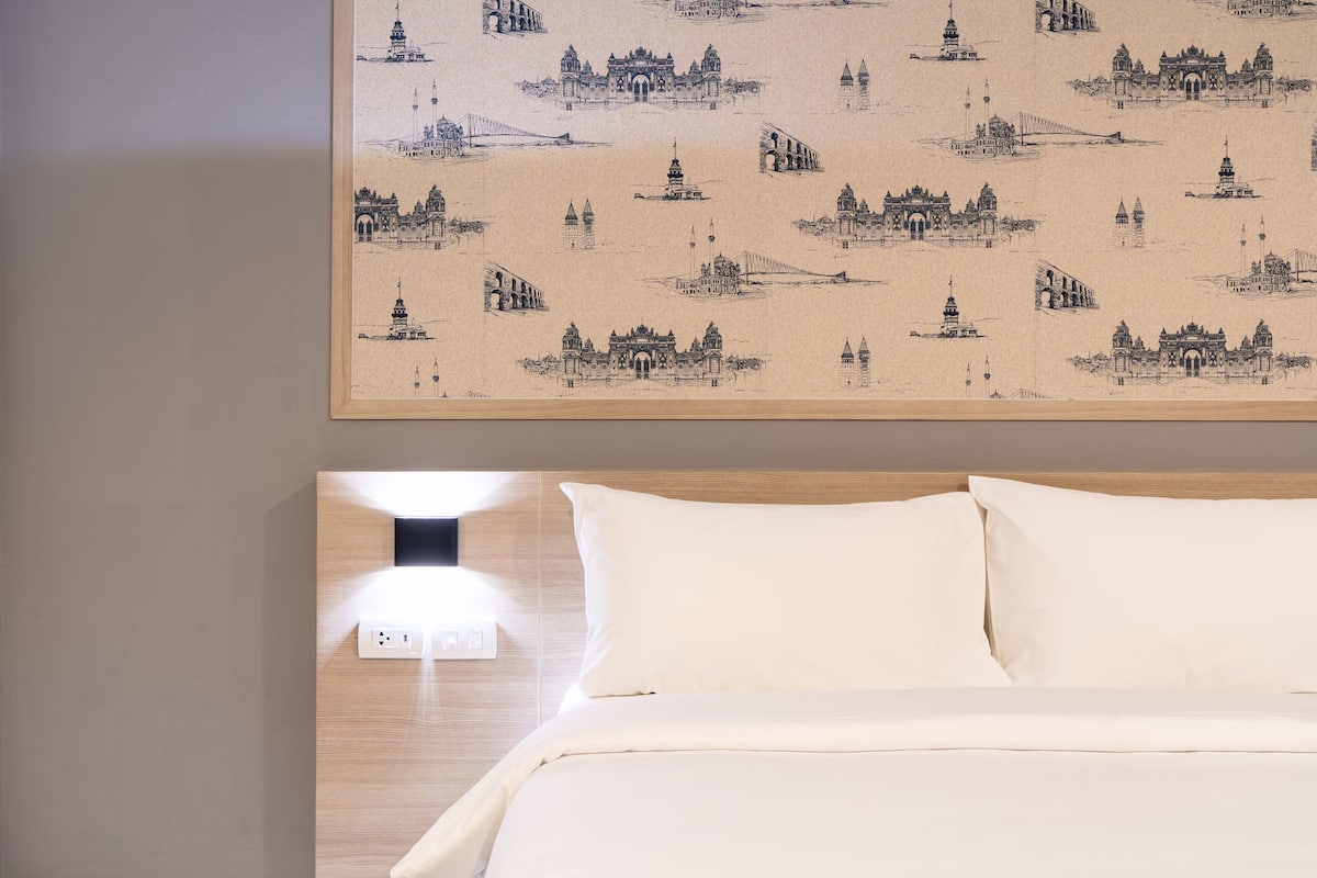A hotel room with a bed, a headboard with a light fixture, and a wall with a patterned artwork.