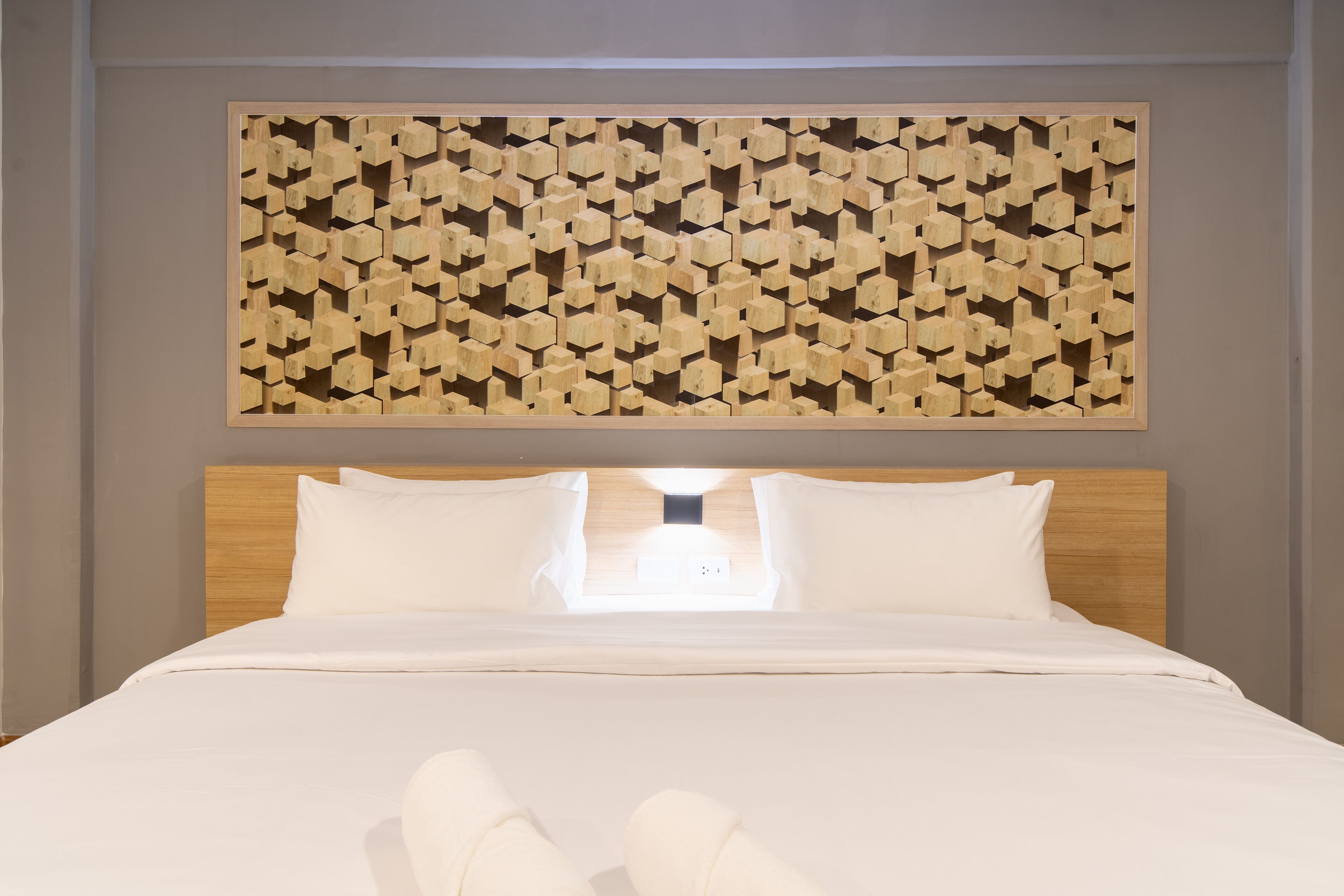 A neatly made bed with white linens and pillows, a wooden headboard, and a geometric wooden wall art piece above it.