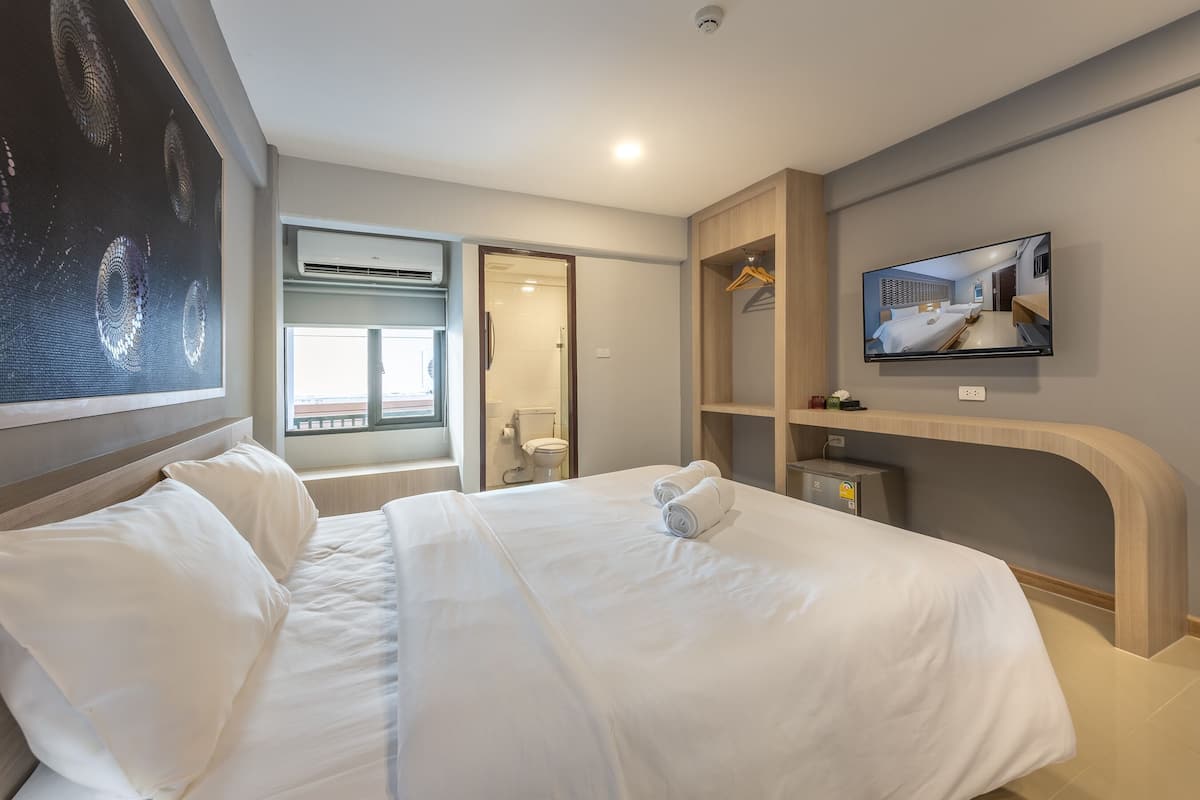 A hotel room with a large bed, a TV mounted on the wall, a wardrobe, and a window with a view.
