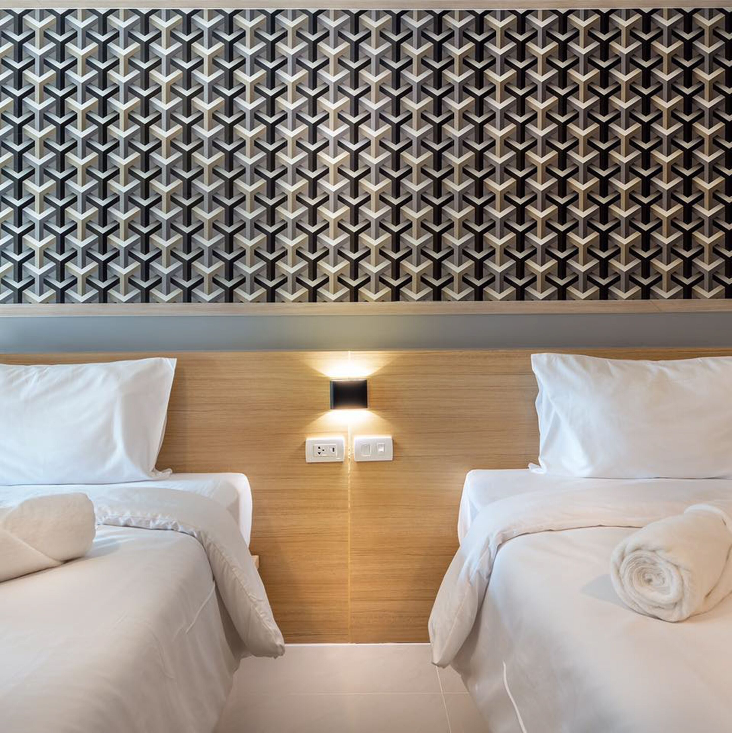 Ein Hotelzimmer mit zwei Betten, einem hölzernen Kopfteil und einer Wand mit geometrischem Muster.