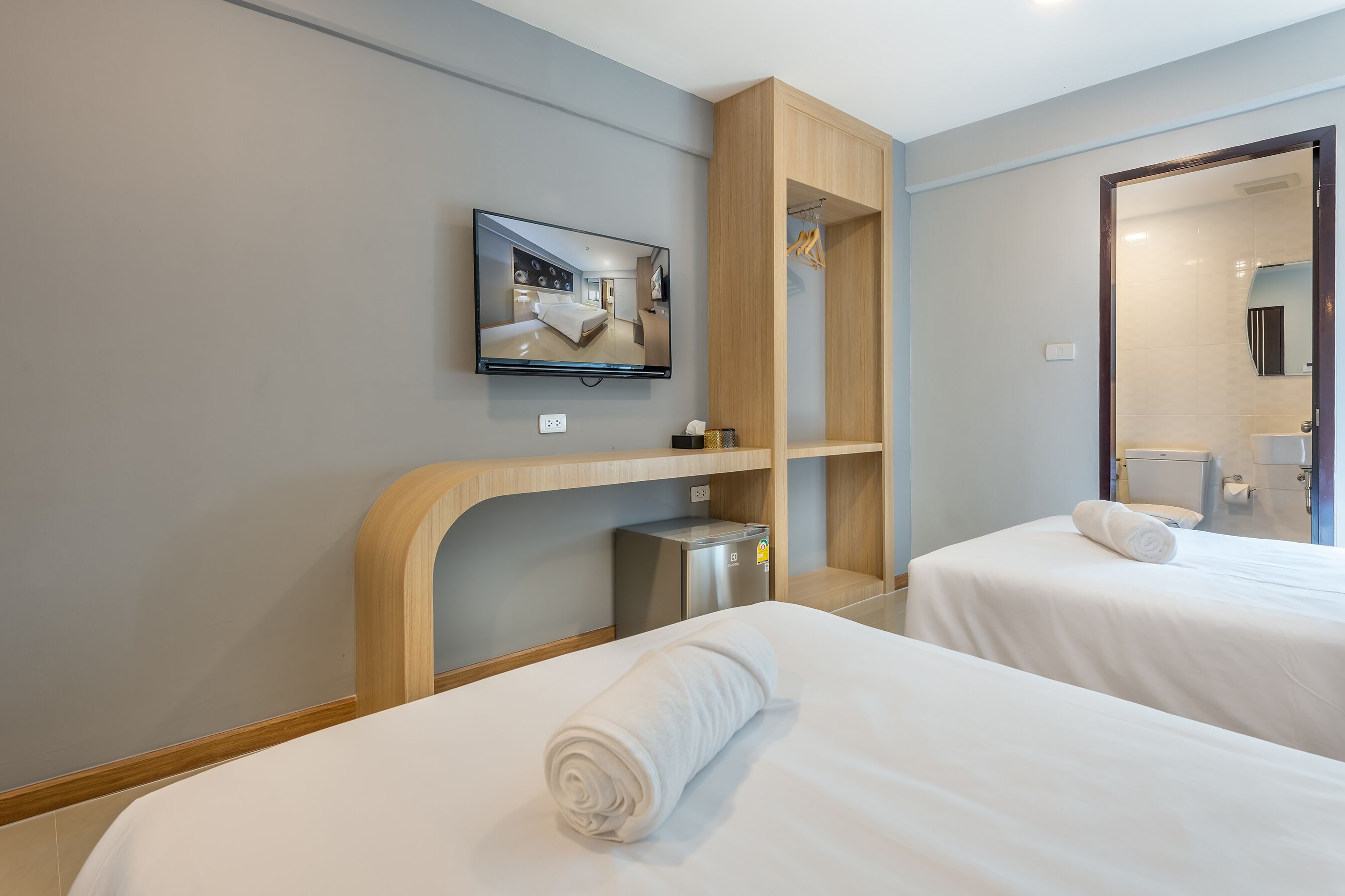 Une chambre d’hôtel avec deux lits, un téléviseur fixé au mur, une armoire en bois et une salle de bain visible à travers une porte ouverte.