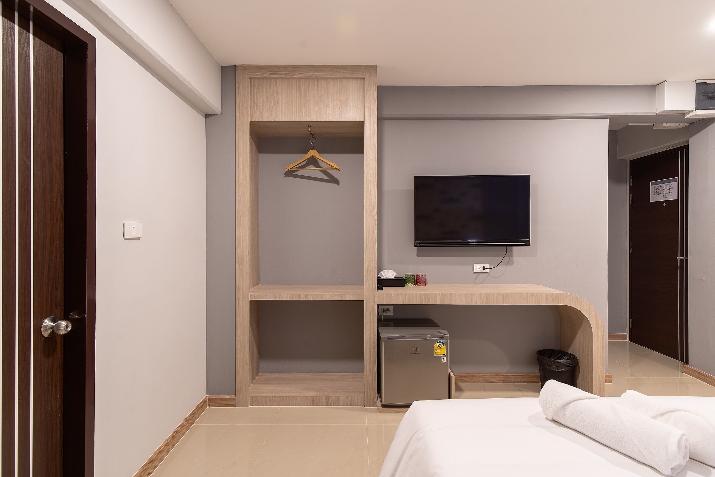 A hotel room with a bed, a TV, a small fridge, a coat rack, and a trash bin.