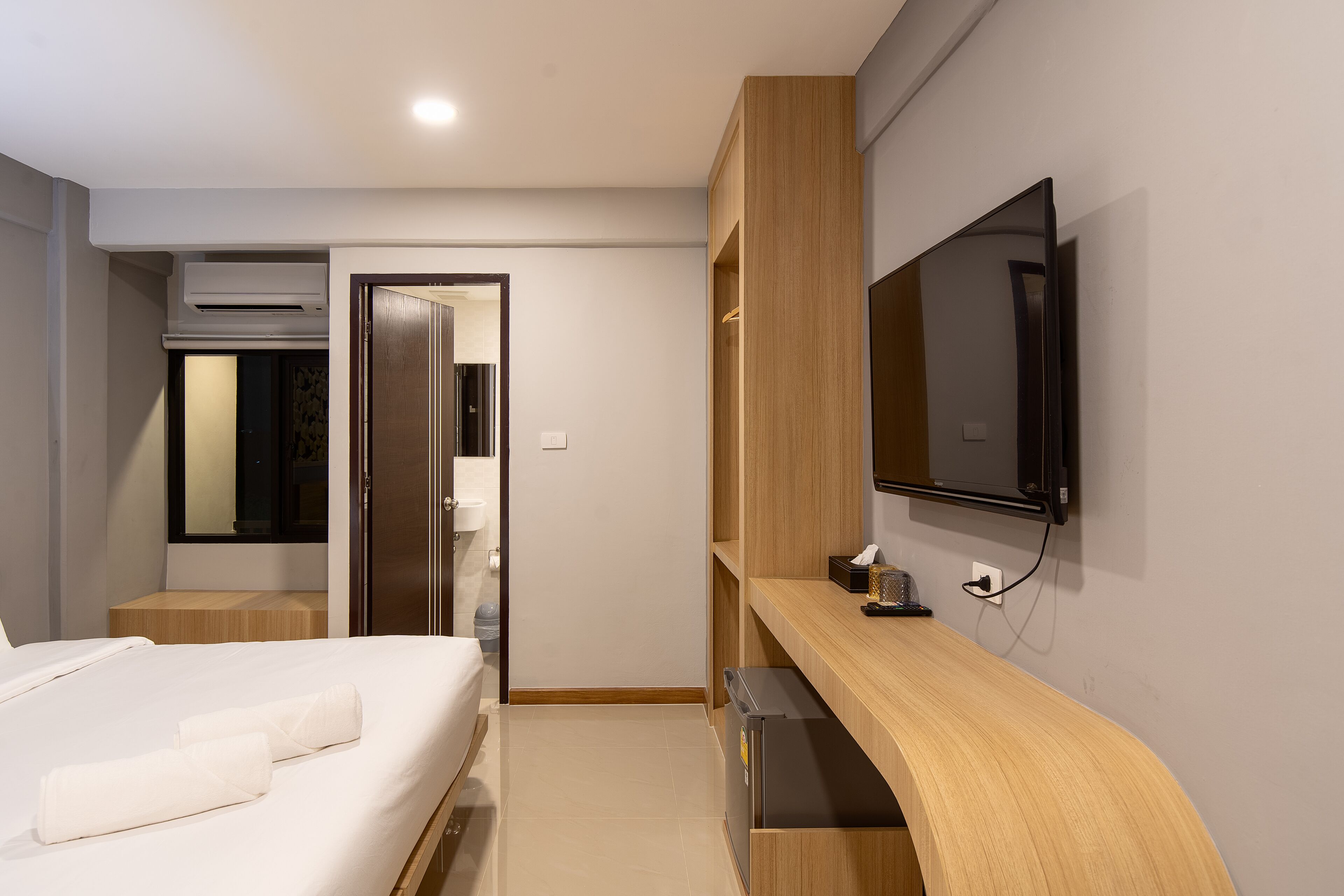 A modern hotel room with a bed, a TV mounted on the wall, a wooden desk, and a built-in wardrobe.