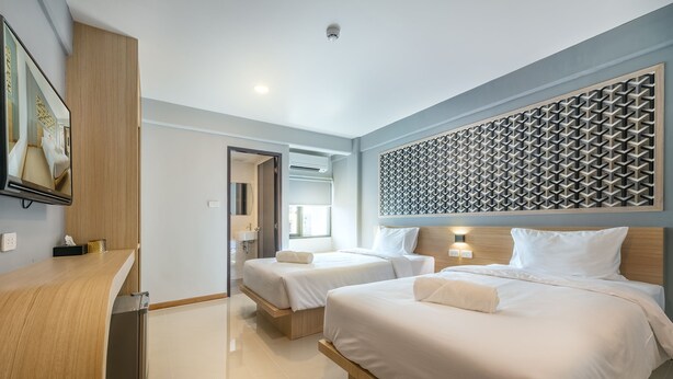 Une chambre d’hôtel moderne avec deux lits, un bureau en bois et un panneau décoratif mural.