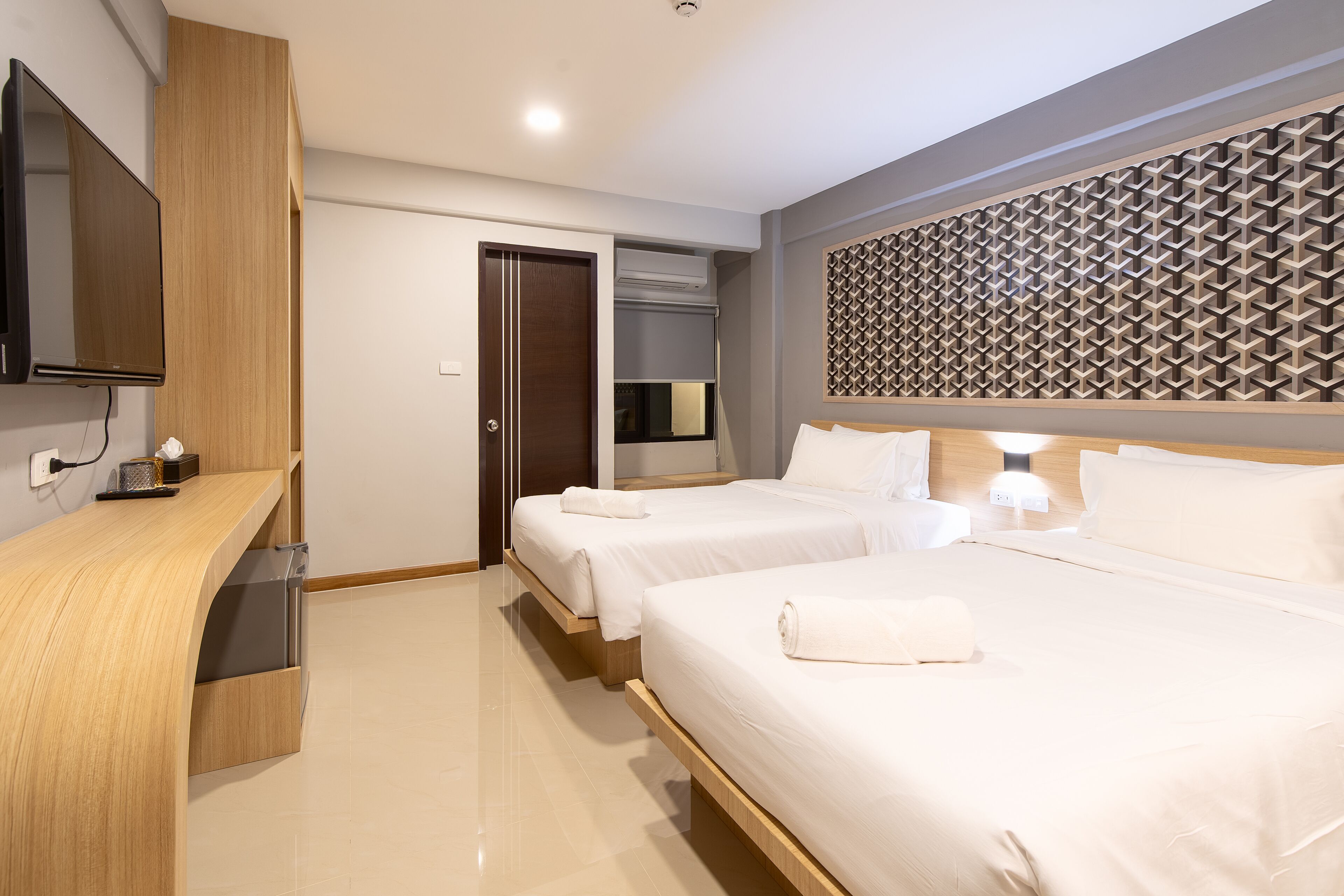 A hotel room with two beds, a wooden desk, a flat-screen TV, and a patterned wall panel.