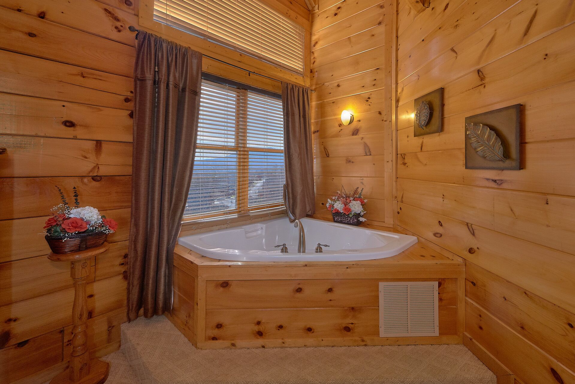 A wooden cabin bathroom with a freestanding bathtub, a window with blinds, and a wall-mounted light fixture.