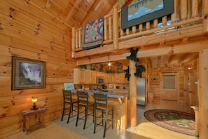 A wooden cabin interior with a kitchen area, bar seating, and a dining table.