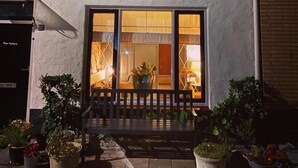 A house with a white exterior, a tiled roof, and a front porch with a bench. There are potted plants on the porch.