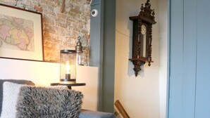 A cozy room with a grey sofa, a hanging plant, a wall-mounted clock, and a framed map.