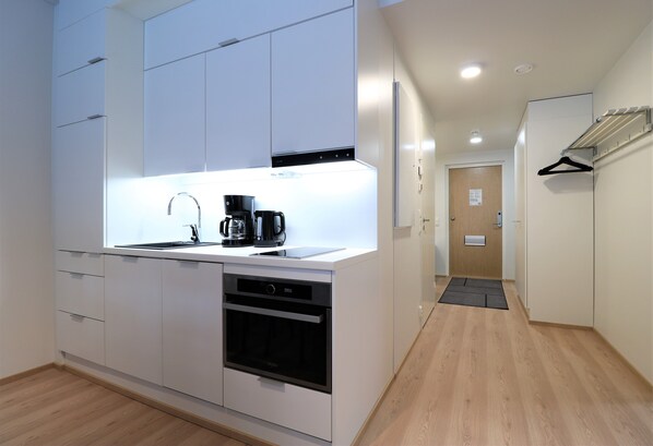 Una cocina moderna con armarios blancos, horno empotrado y cafetera.