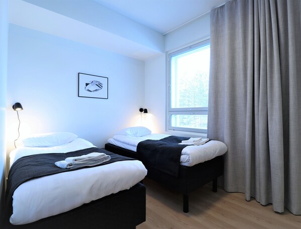 A hotel room with two beds, a window with curtains, a wall-mounted lamp, and a framed picture.