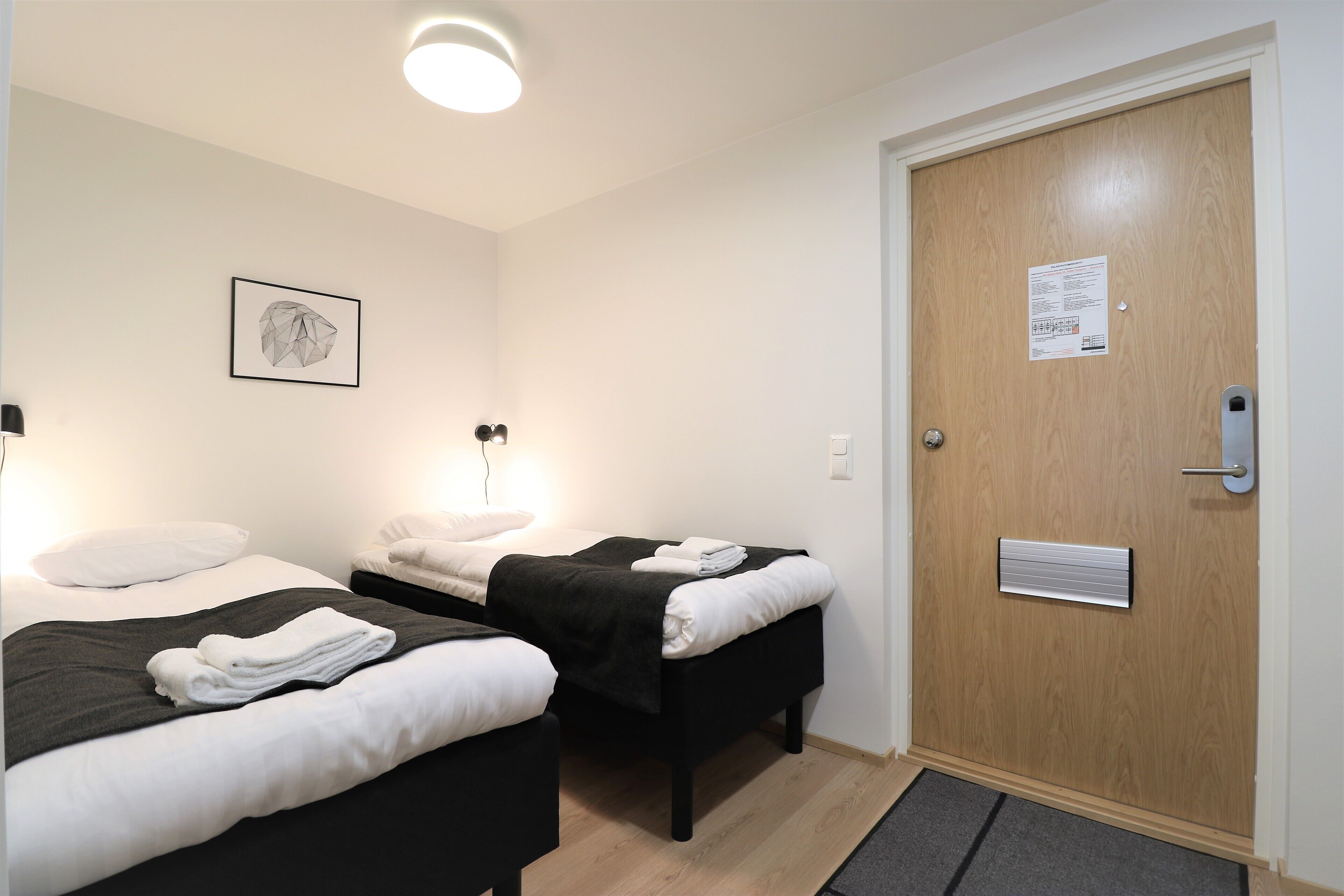 A hotel room with two beds, a wooden door, and a framed picture on the wall.
