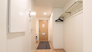 Un couloir étroit doté d’un plancher en bois, une porte au fond et un porte-manteau sur le mur de droite.