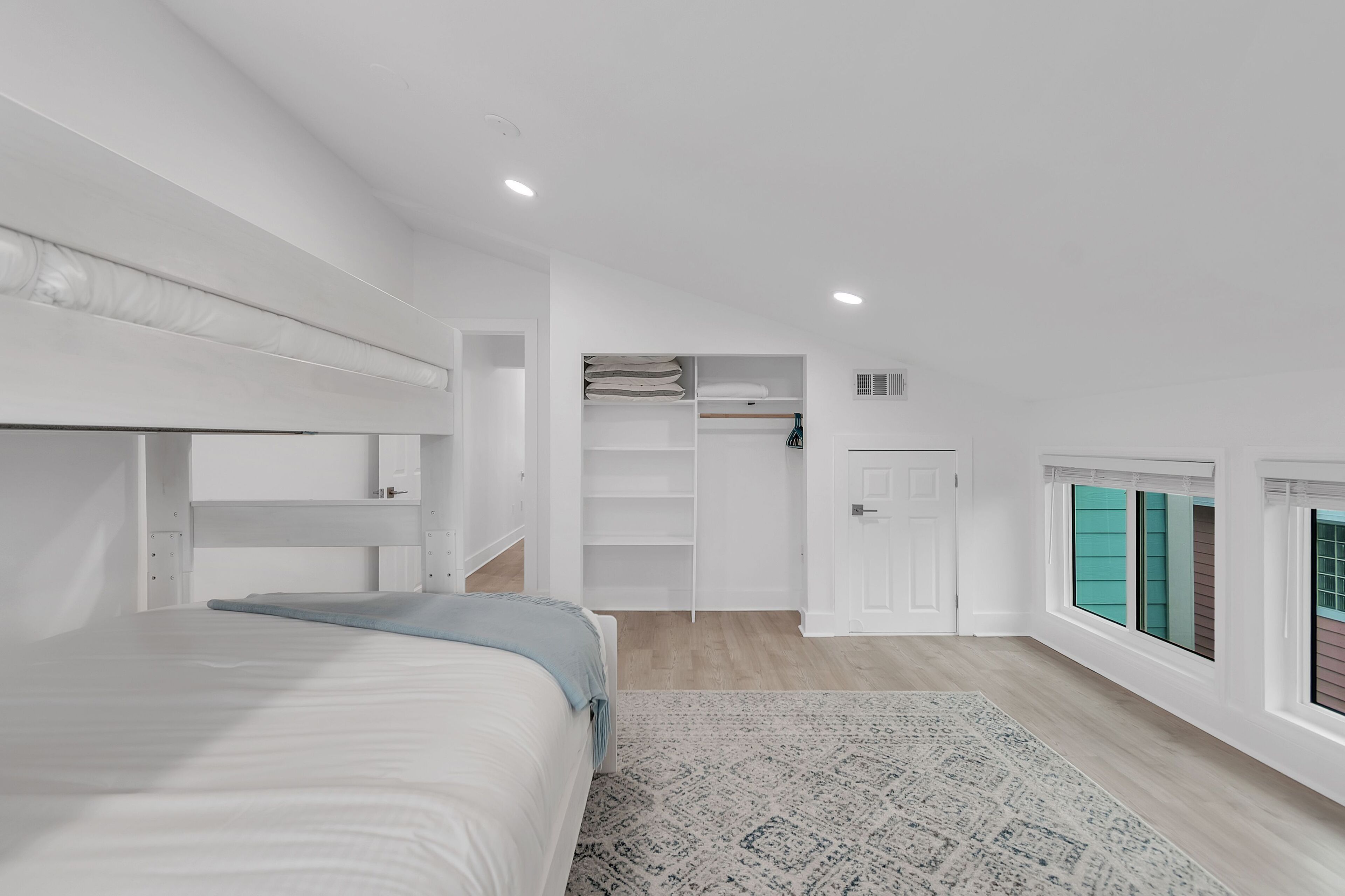 Une chambre moderne avec un lit superposé, un dressing et une vue par une fenêtre dotée de volets.