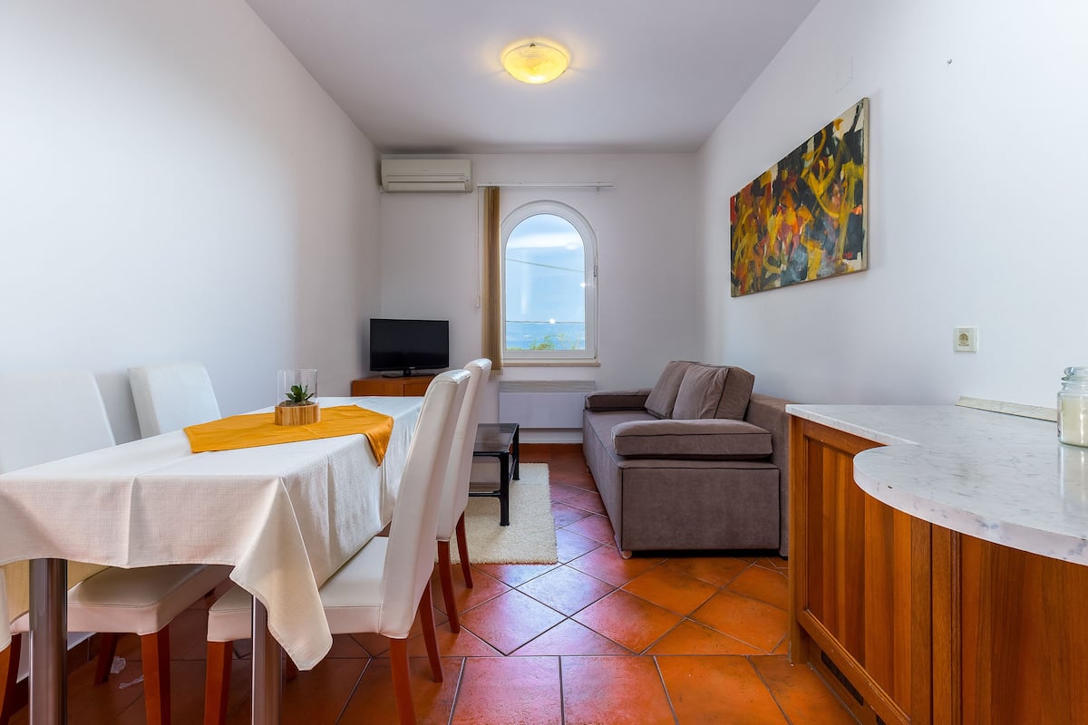 A compact living space with a dining area, a sofa, a TV, and a window with a view.
