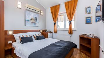 Una habitación de hotel con cama, mesita de noche, cómoda, ventana con cortinas, televisor montado en la pared y obras de arte.