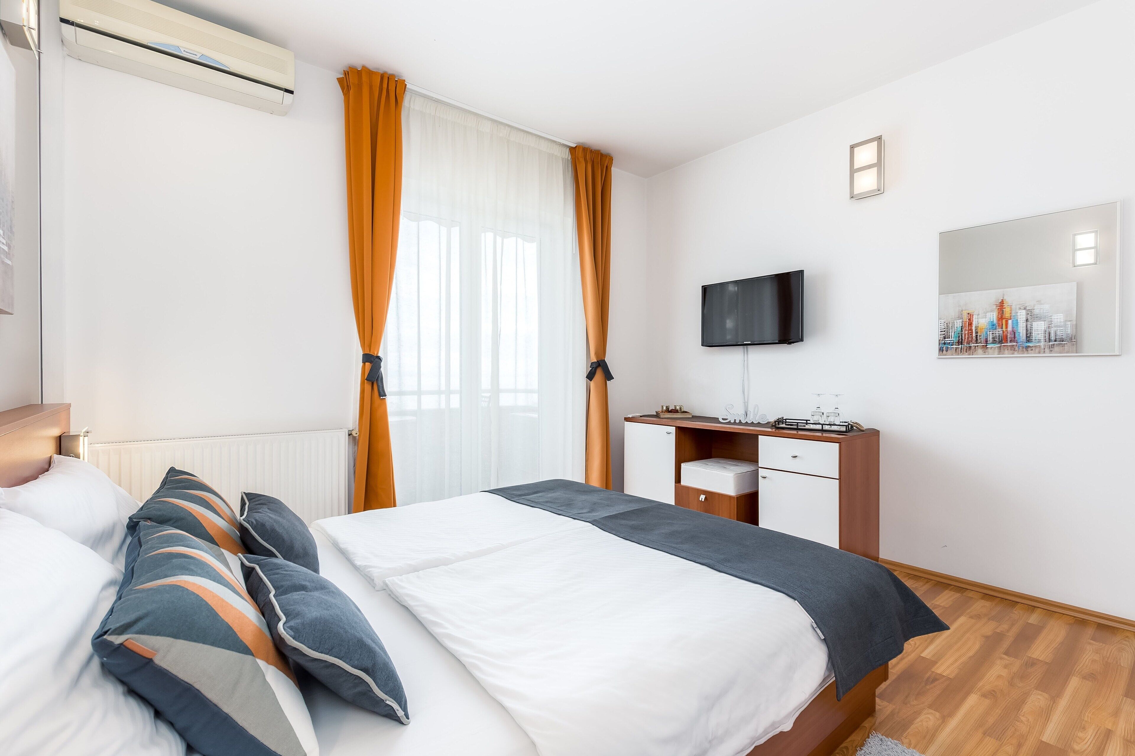 A hotel room with a bed, a desk, a flat-screen TV, and a cityscape painting on the wall.