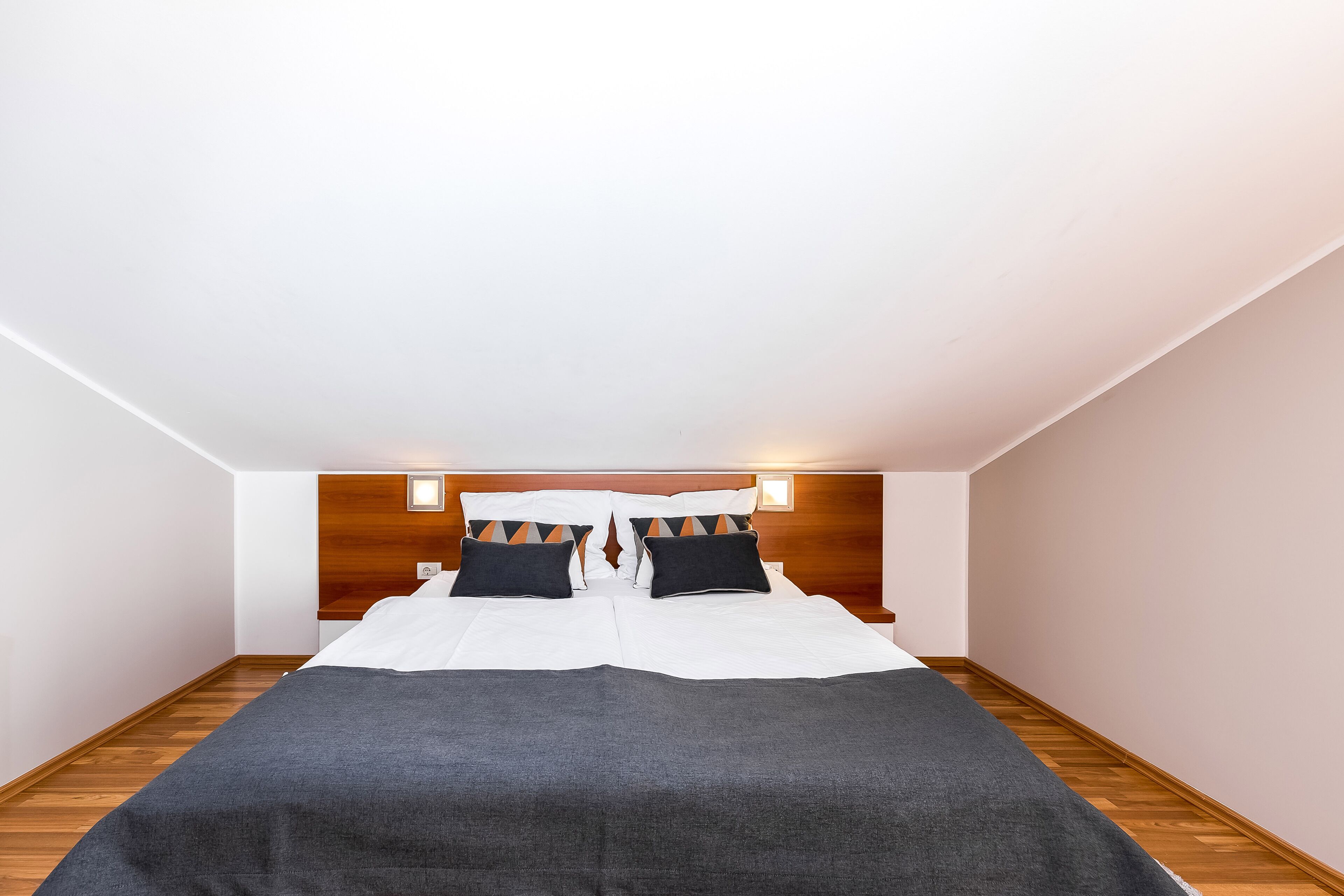 A modern hotel room with a large bed, wooden headboard, and a small bedside table.