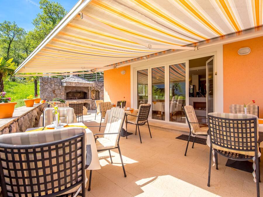 Un patio exterior con toldos a rayas, chimenea de piedra y varias zonas de estar.
