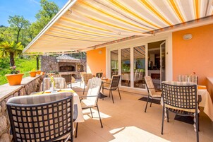 Un patio exterior con toldos a rayas, chimenea de piedra y varias zonas de estar.