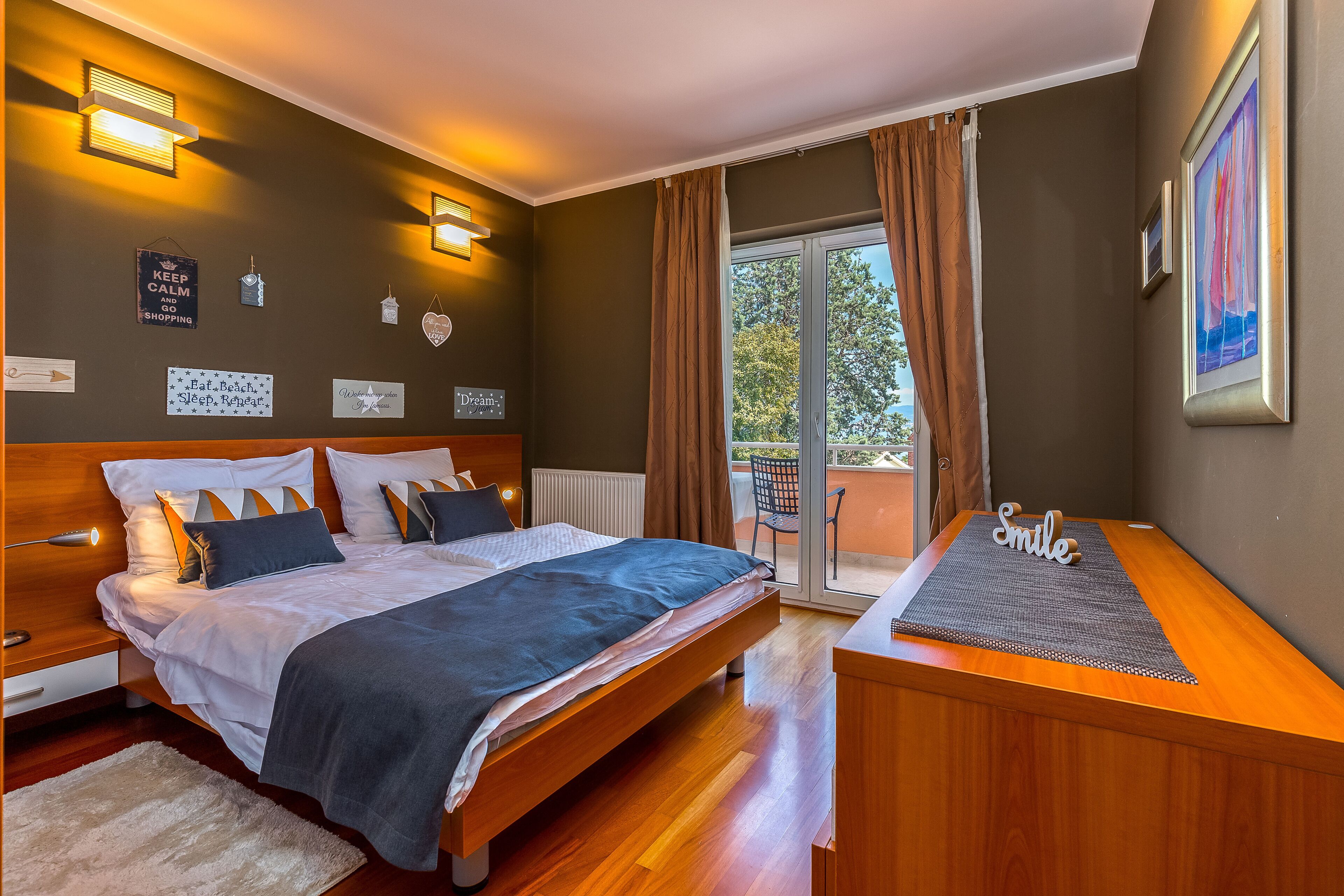 A bedroom with a bed, bedside tables, a desk, and a view of the outdoors.