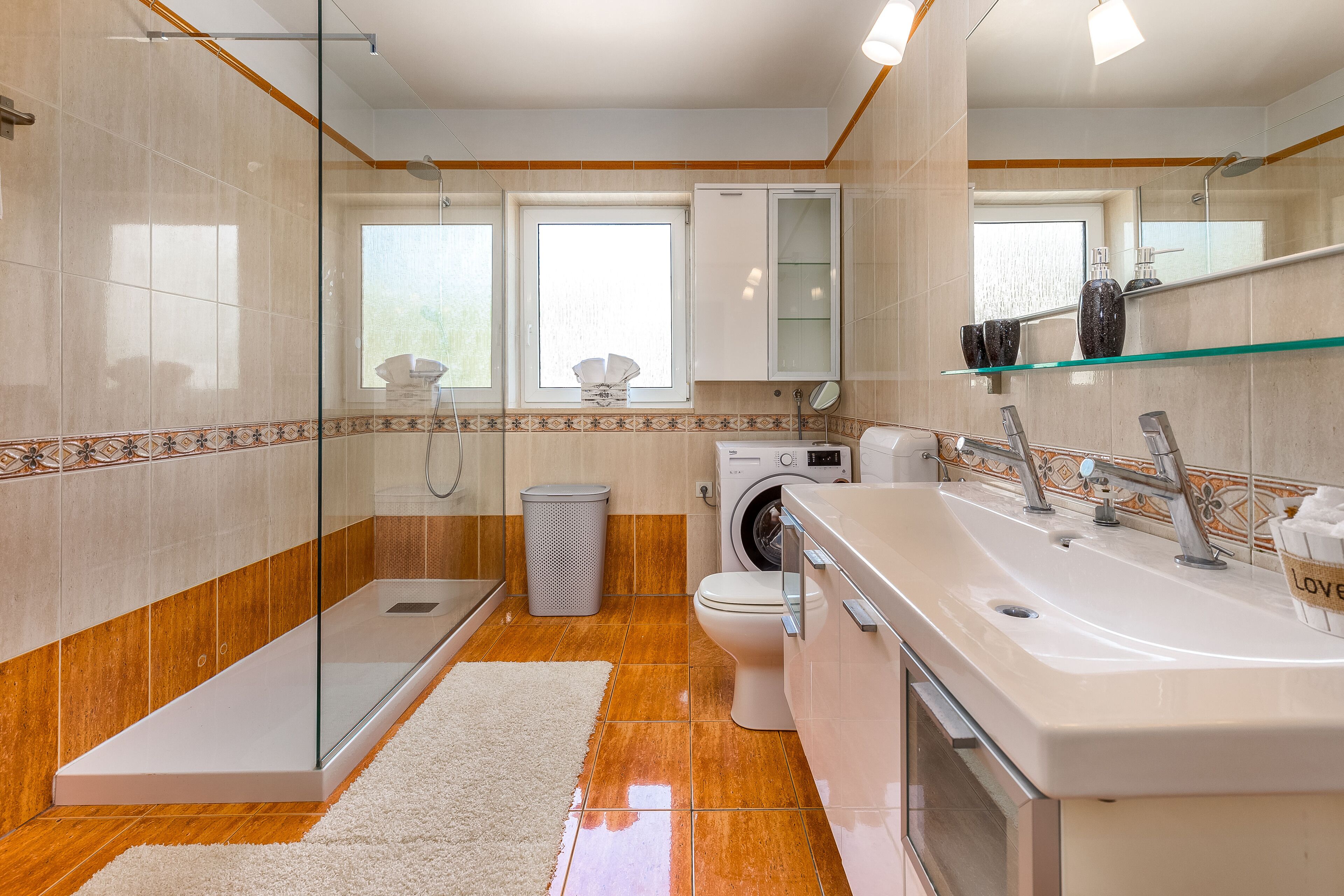 Un baño moderno con cabina de ducha de vidrio, lavadora integrada, inodoro y un lavamanos grande con espejo.