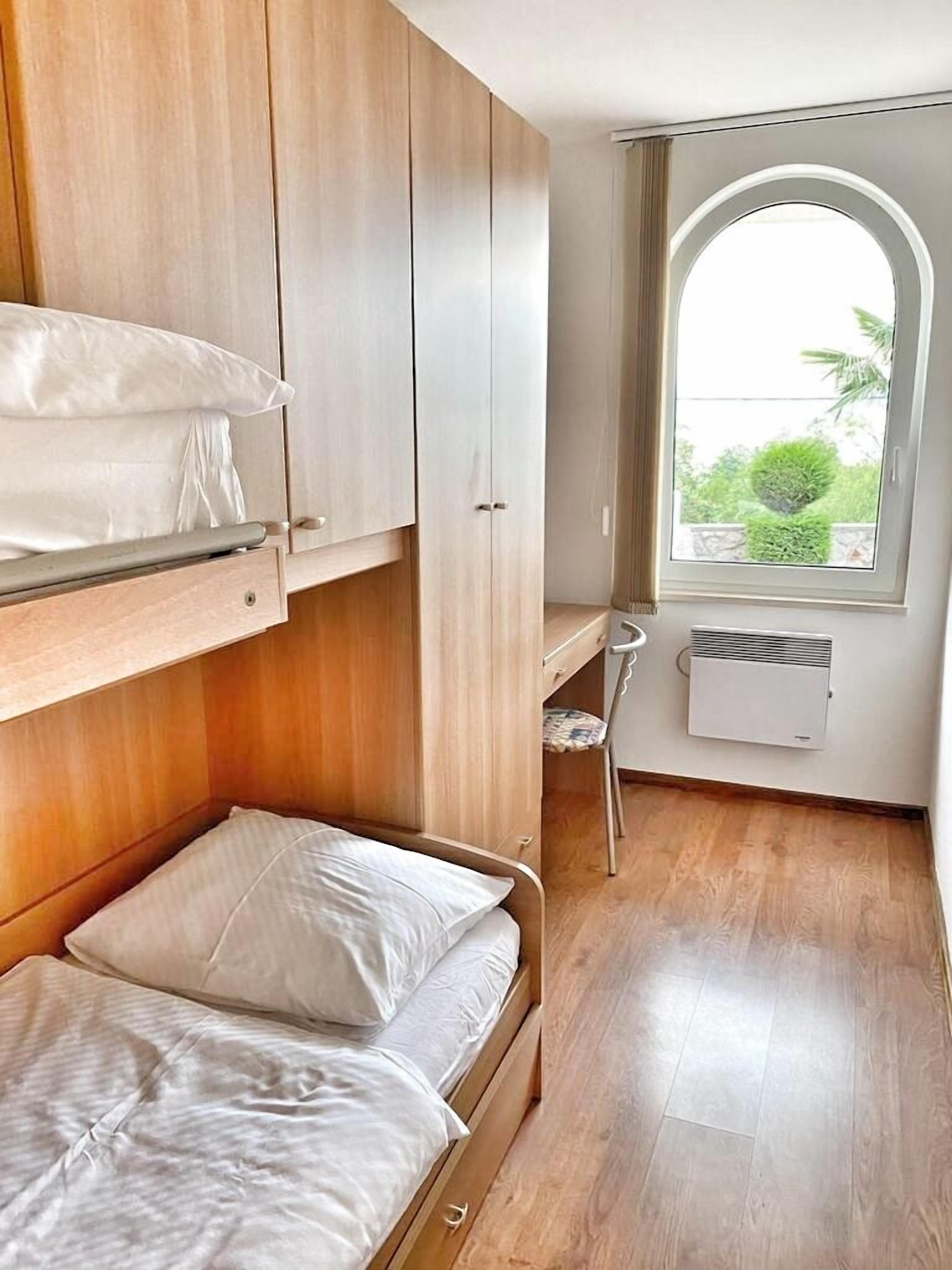 A compact bedroom with a bunk bed, a small desk, and a window with a view of greenery.