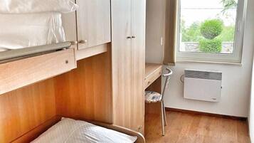 A compact bedroom with a bunk bed, a small desk, and a window with a view of greenery.