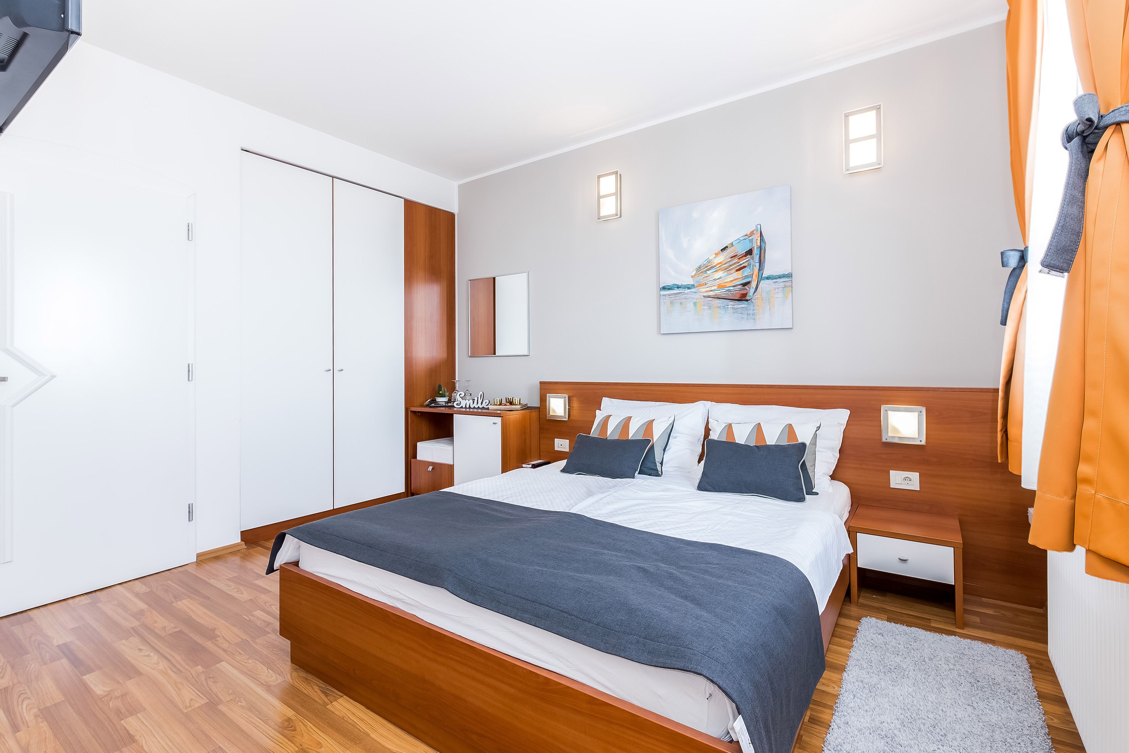Un dormitorio moderno con una cama de madera, paredes blancas, un cuadro y una mesita de noche.