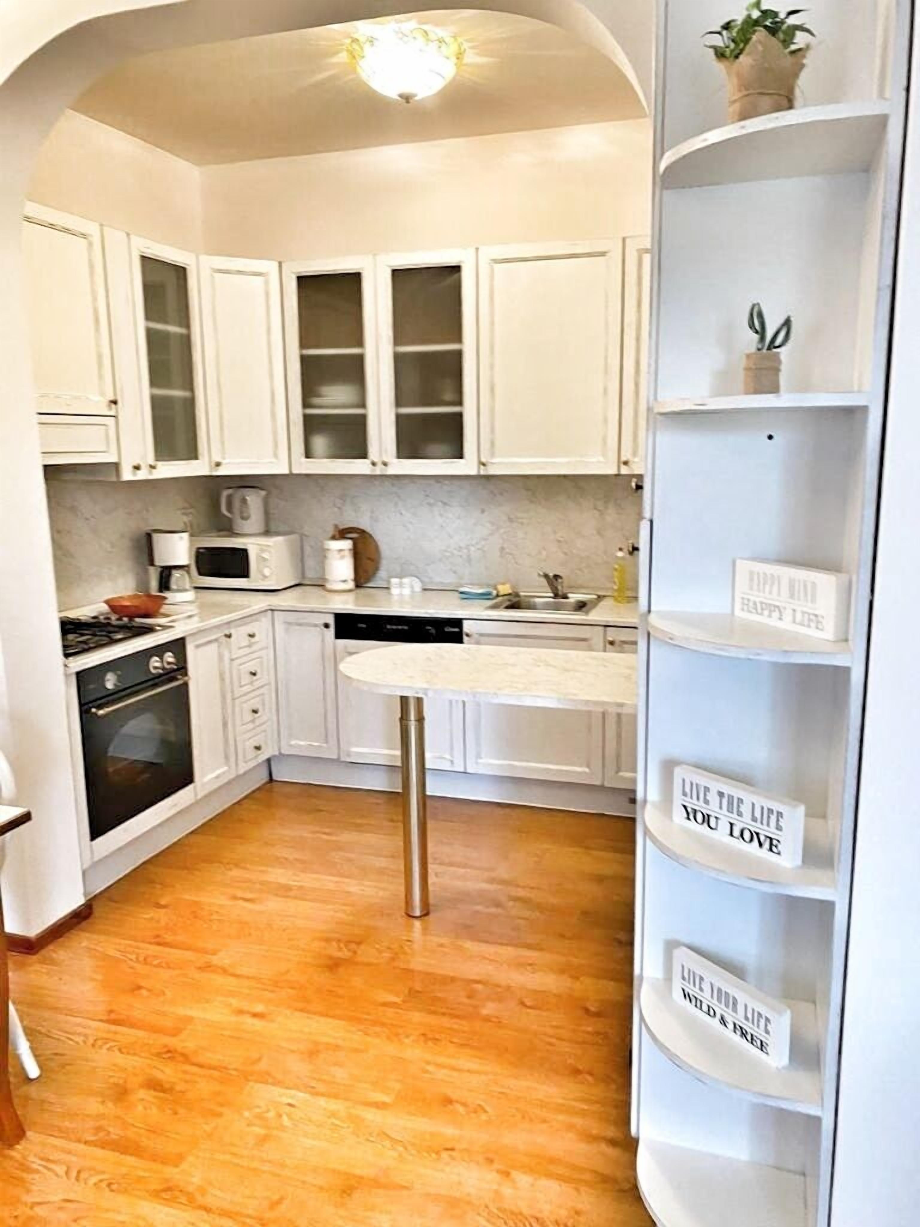 A kitchen with white cabinets, a microwave, a stove, and a sink. There is a shelf with motivational signs.