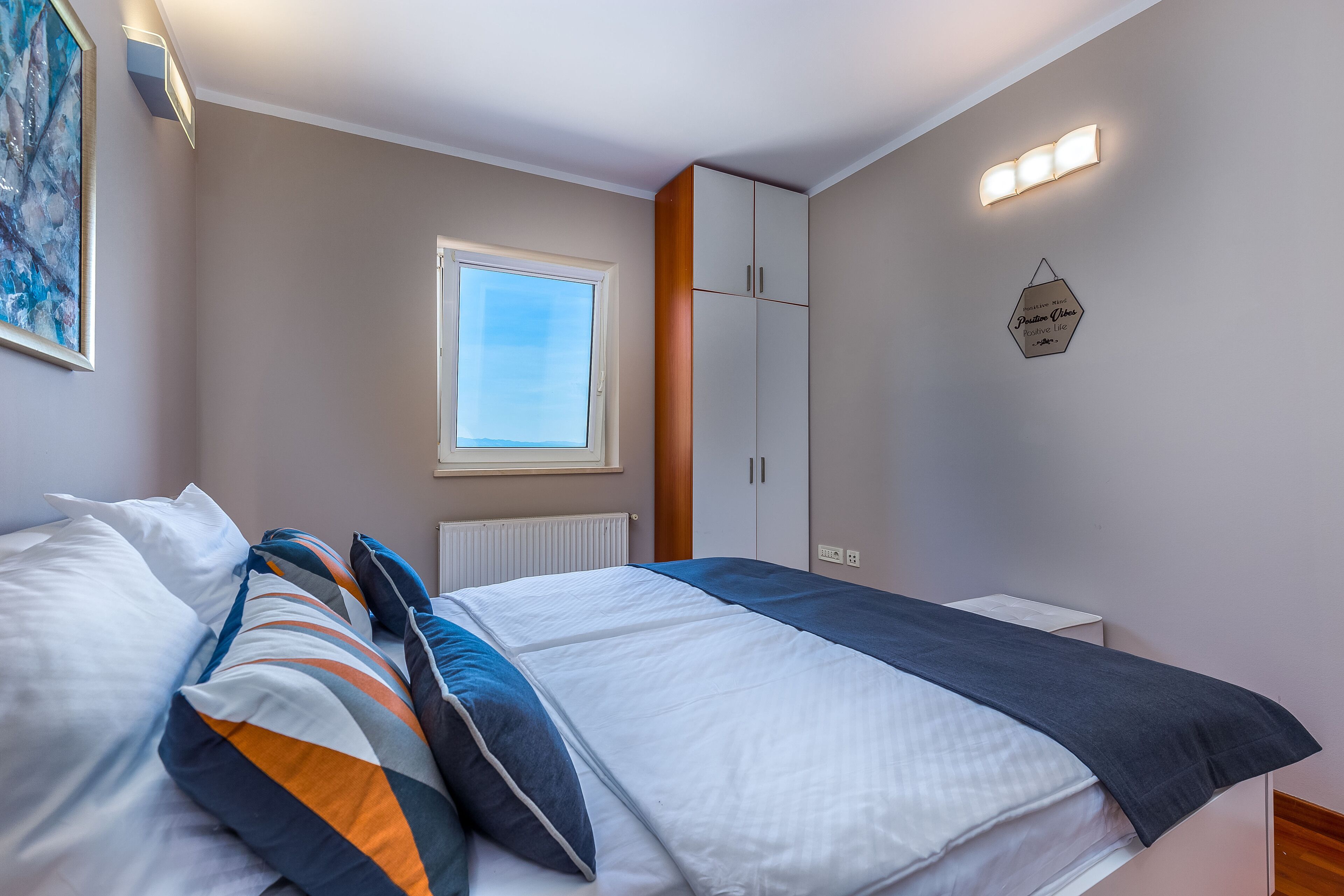 Un dormitorio con cama, ventana, armario y una lámpara fijada a la pared.