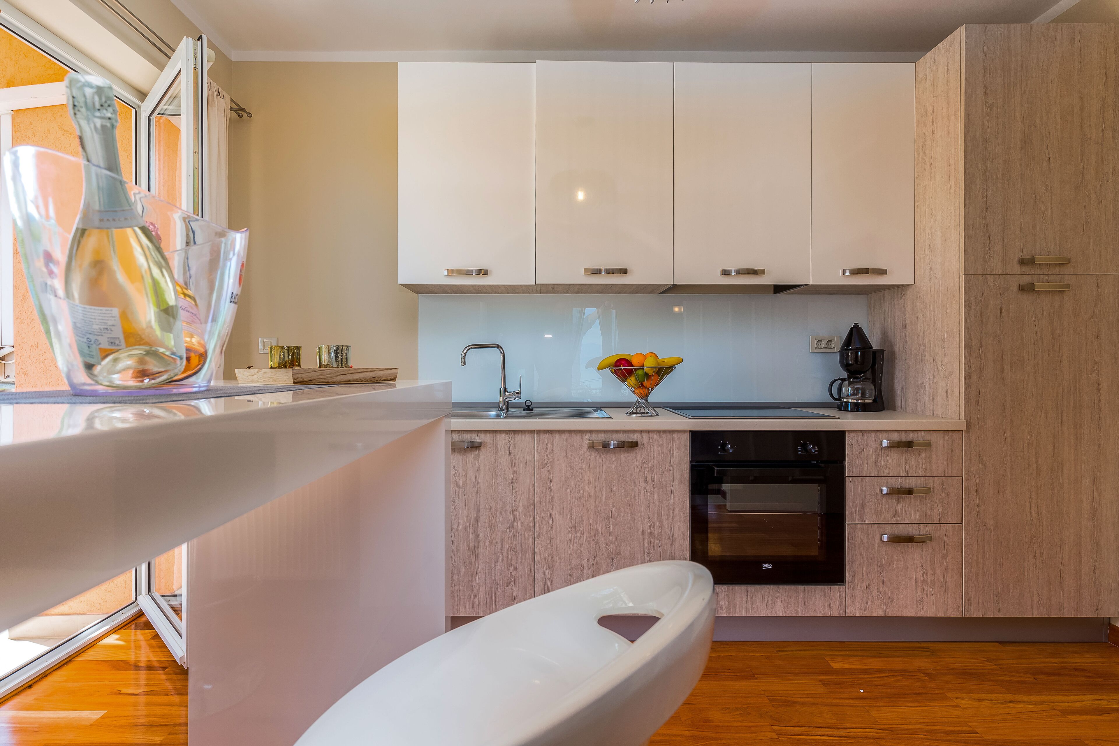 A modern kitchen with white cabinets, a built-in oven, and a large window.