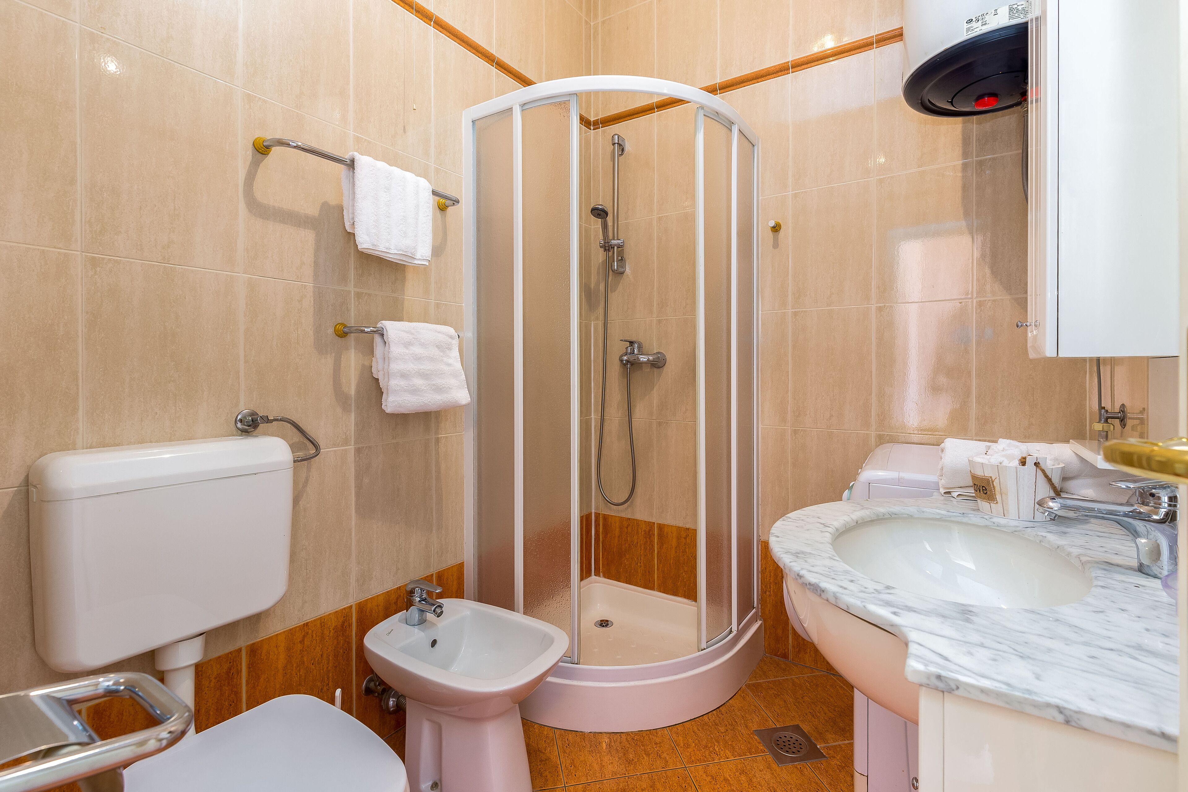 Een badkamer met een douchecabine, een toiletbril, een toilet en een wastafel met een marmeren blad.