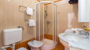 Een badkamer met een douchecabine, een toiletbril, een toilet en een wastafel met een marmeren blad.