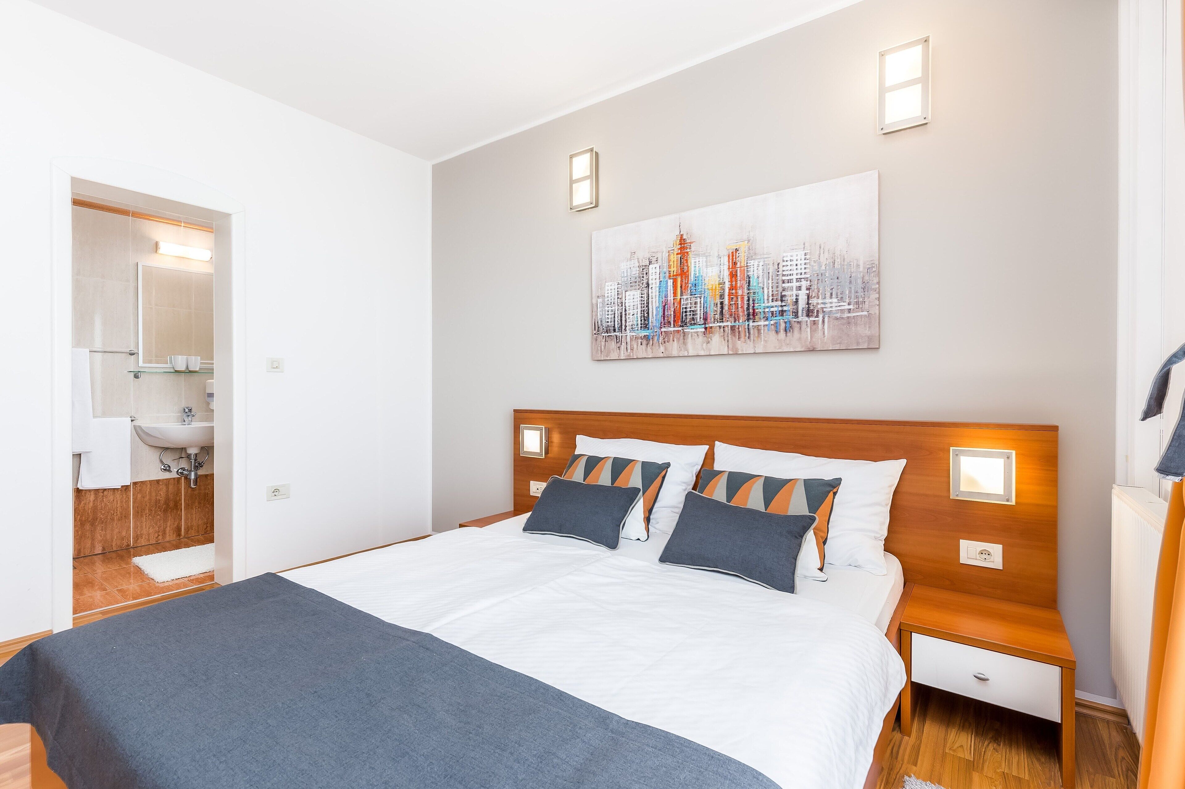 Quarto de hotel moderno com cama grande, cabeceira de madeira e uma pintura da paisagem urbana.