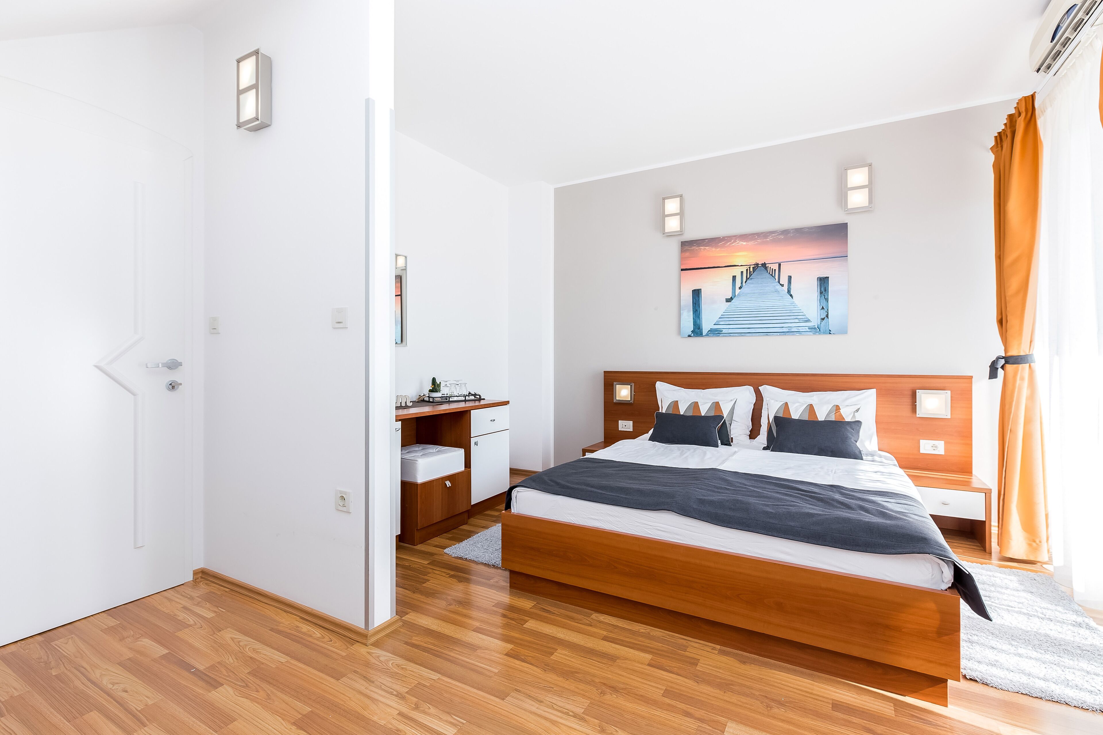 A modern bedroom with a wooden bed, a desk, and a painting on the wall.