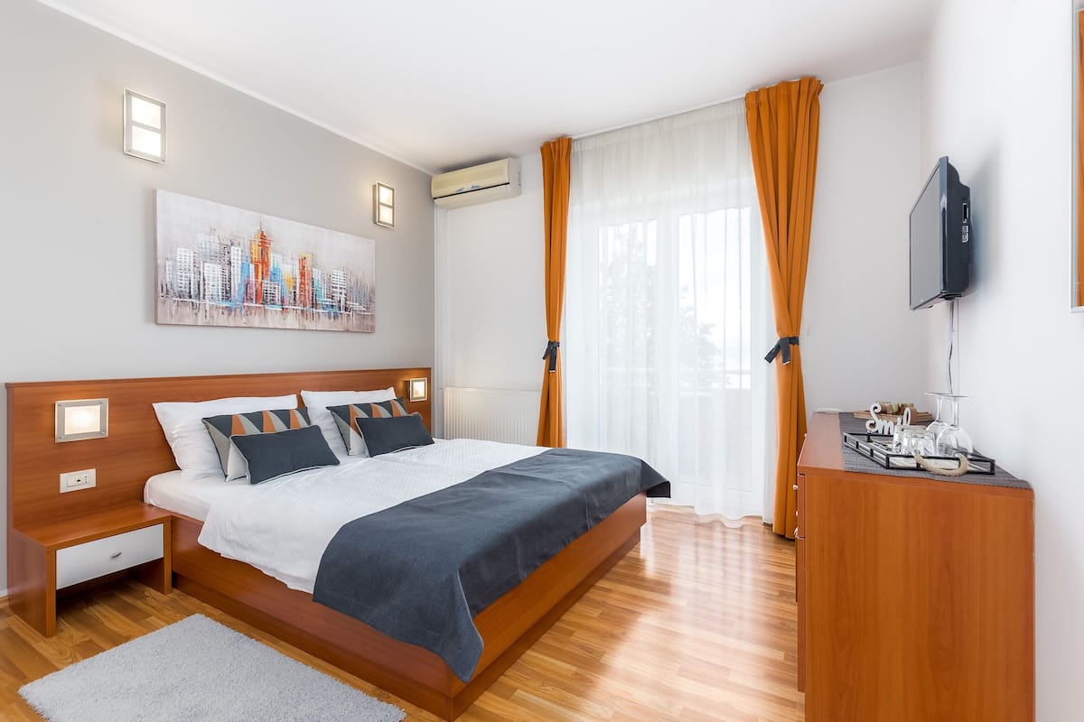 A modern bedroom with a wooden bed, a nightstand, a desk, and a cityscape painting on the wall.